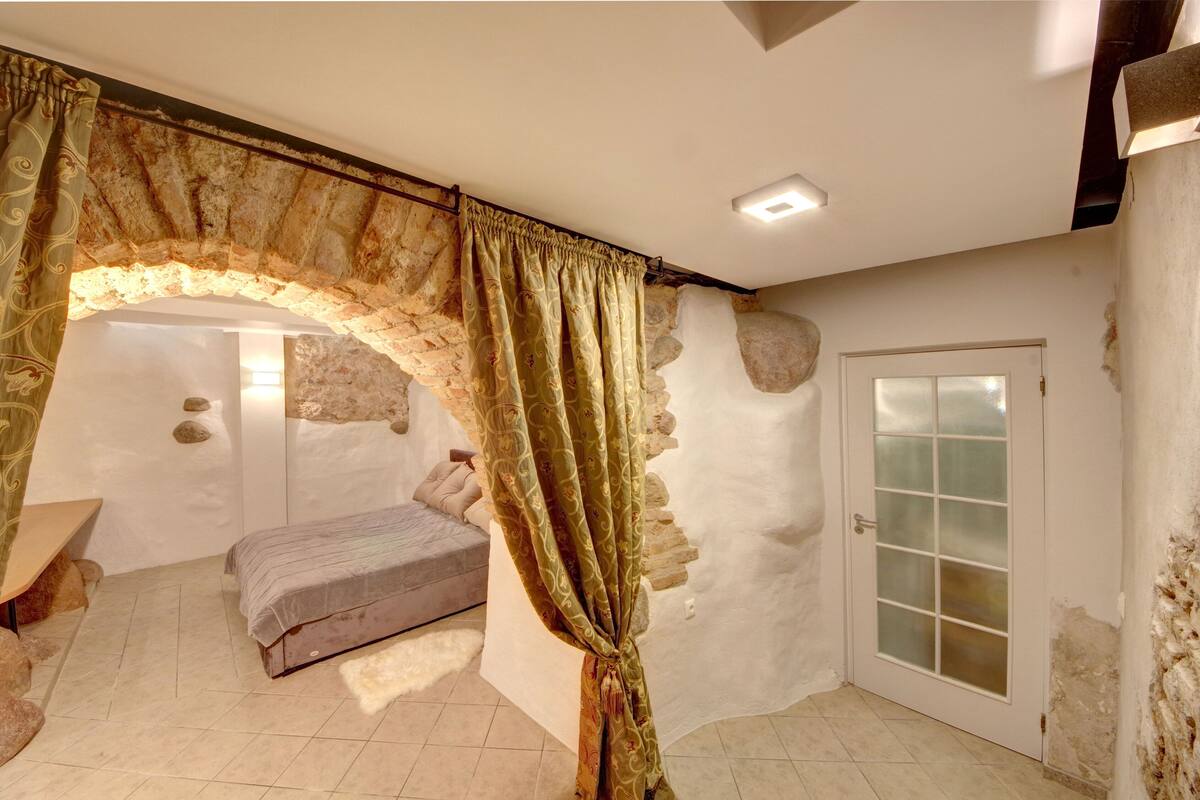 A bedroom with a stone archway, a bed, a bench, and a door with frosted glass panels.