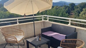 A balcony with wicker furniture, a table with a bottle and glass, and a large umbrella. - APARTMENT 4/6 PERS (Oletta)