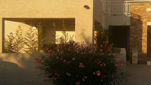 A two-story building with a balcony, a small garden with pink flowers, and a clear sky. - APARTMENT 4/6 PERS (Oletta)
