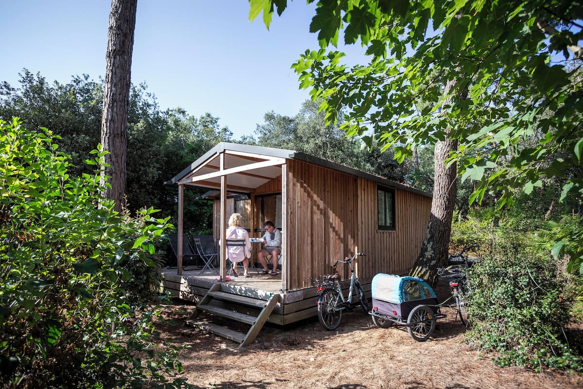 A wooden cabin with a porch, a bicycle, and a covered bike rack.
