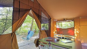 Ein Zelt mit Tisch und Stühlen, ein Hut hängt an einem Stuhl, und im Hintergrund sind Bäume zu sehen.