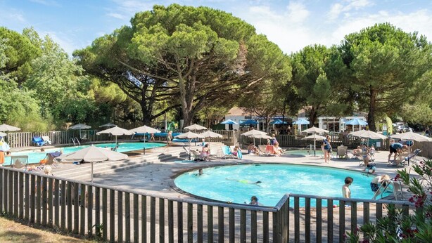 Ein Poolbereich mit mehreren Schwimmbecken, Liegestühlen, Sonnenschirmen und einer Holzterrasse.