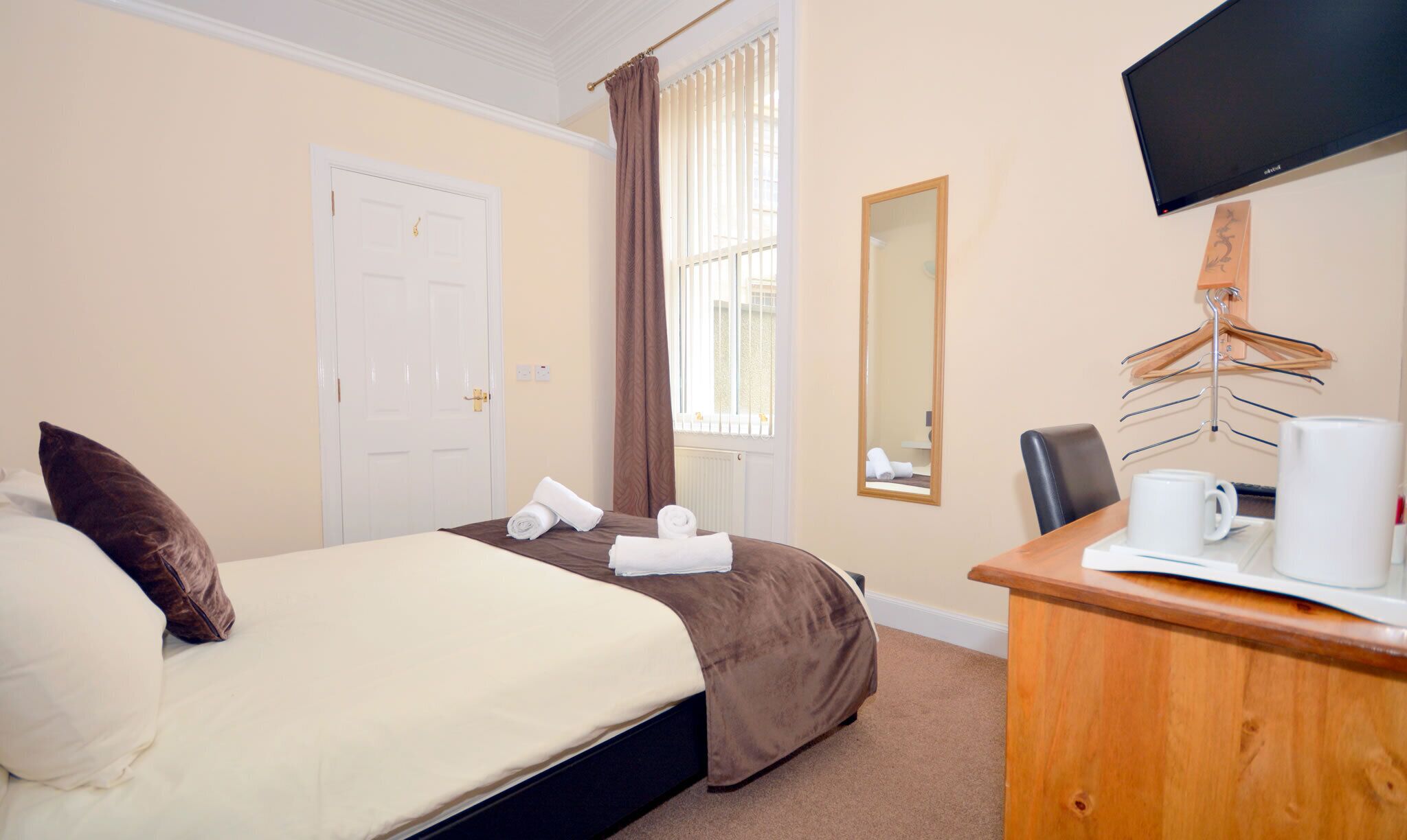 A hotel room with a bed, a desk with a chair, a television, and a window with curtains.
