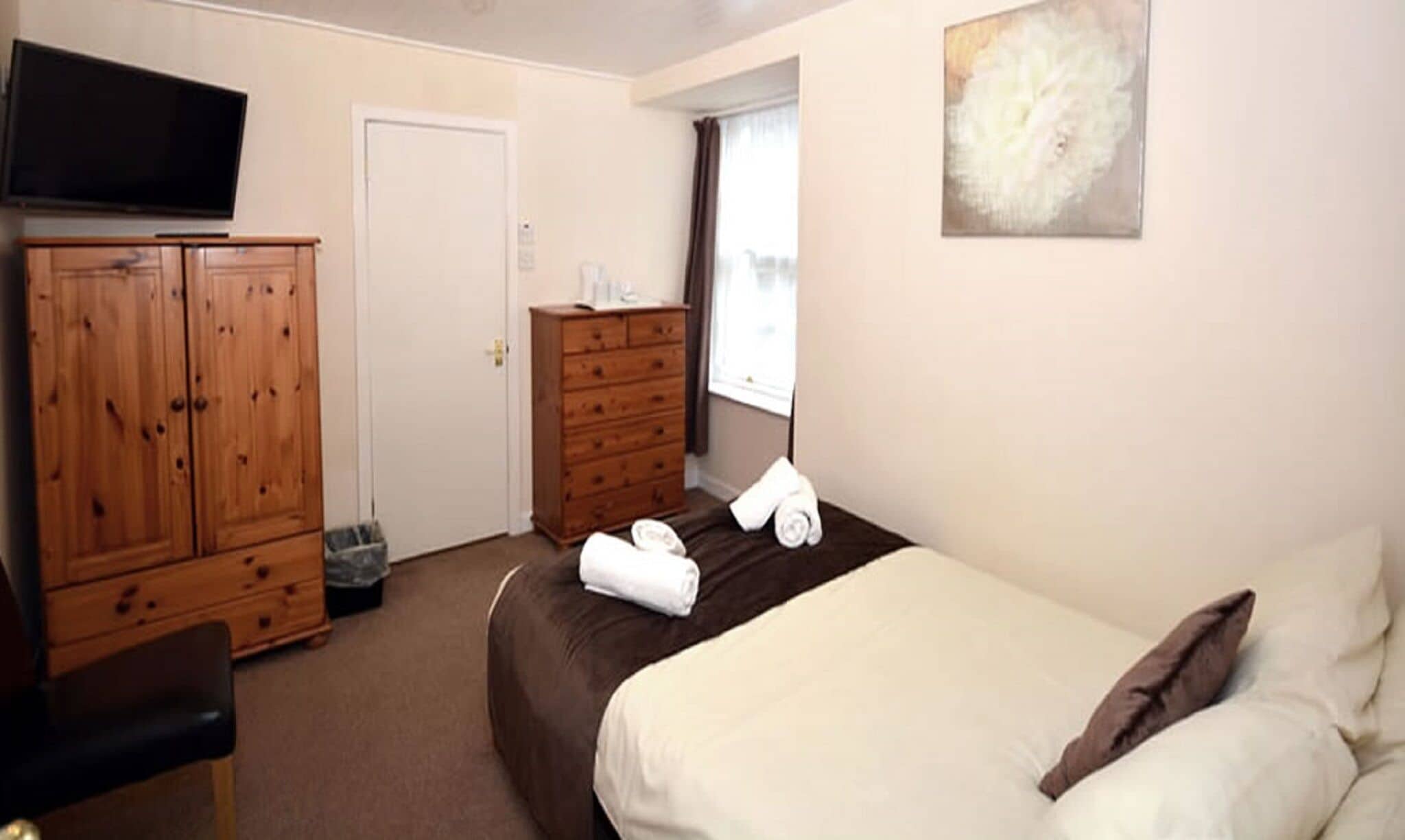 Un dormitorio con una cama, un armario de madera, un televisor y una ventana.