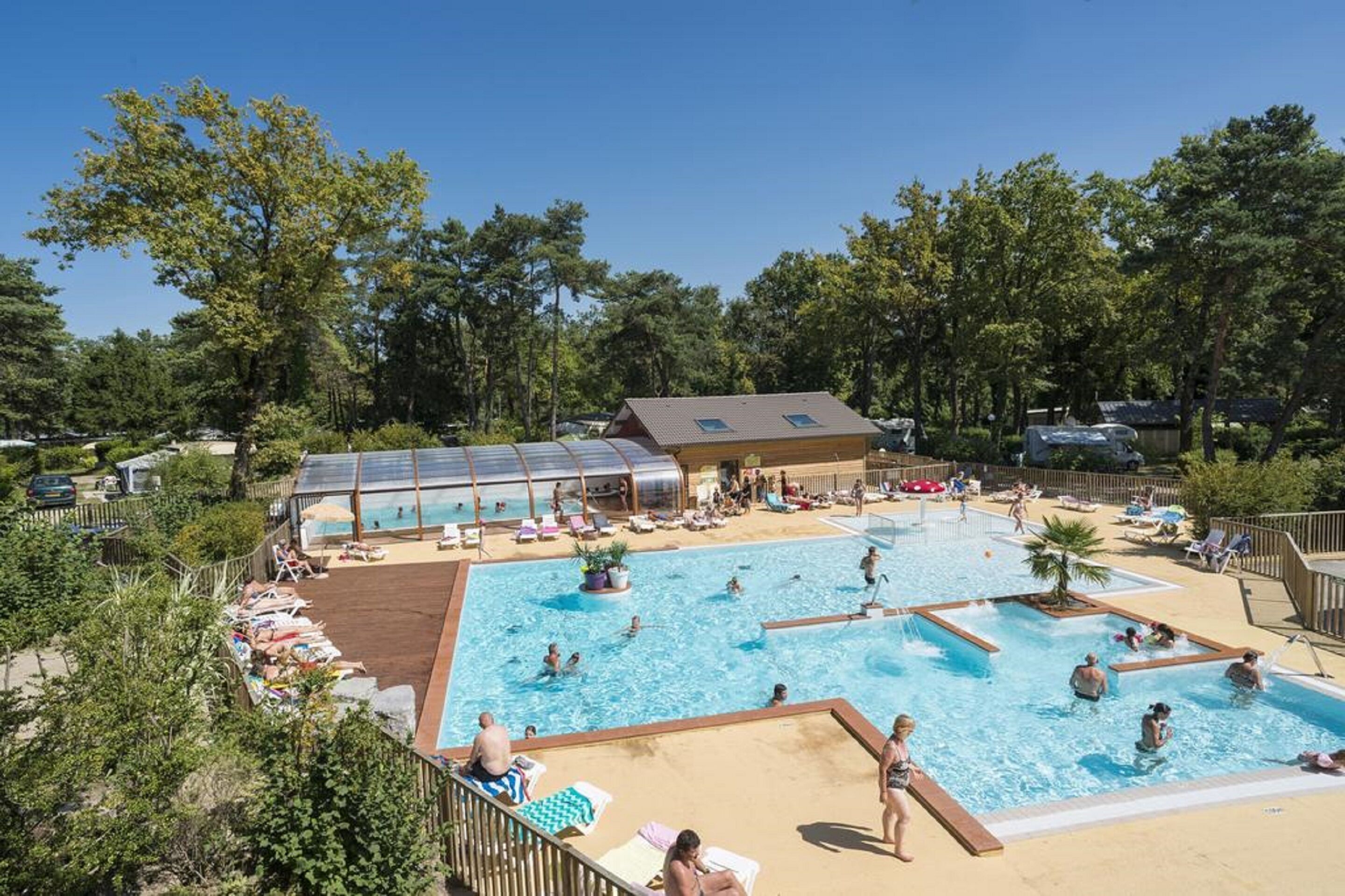 Zona de piscina con varias piscinas, tumbonas y un área de descanso cubierta.