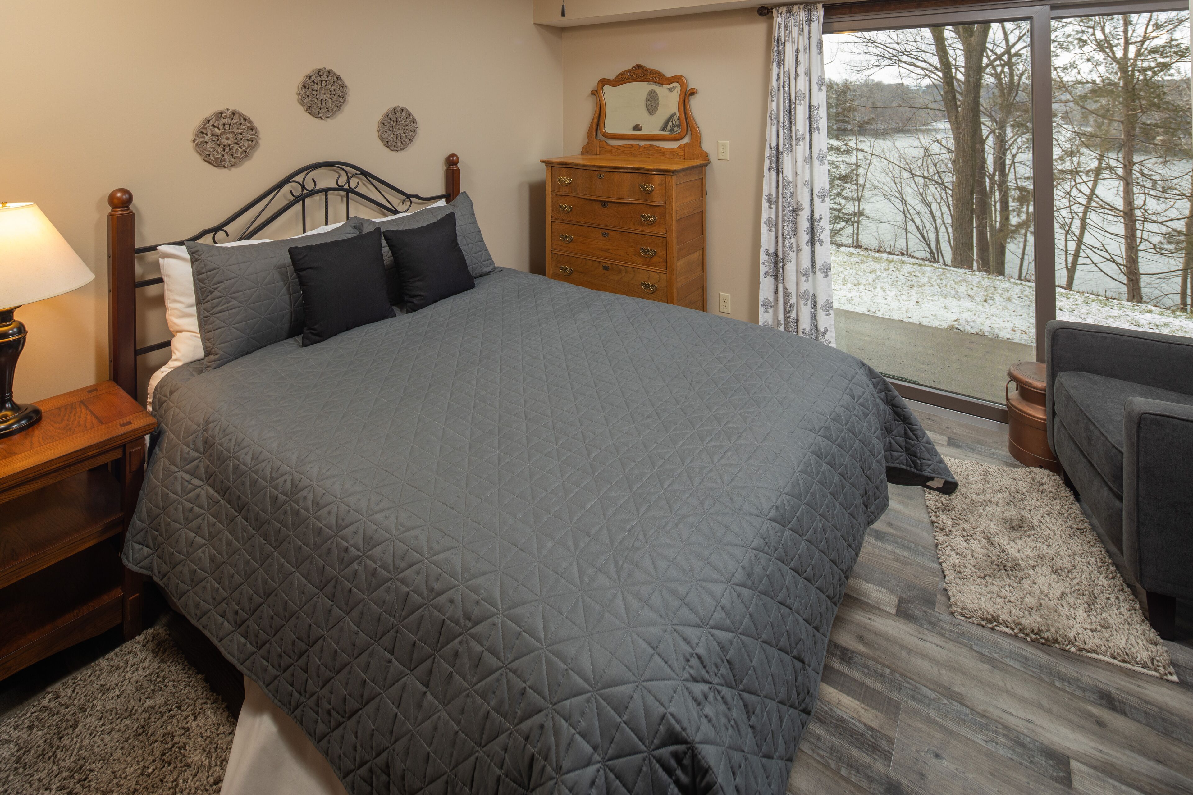 Ein Schlafzimmer mit einem großen Bett, einer Holzkommode, einem Nachttisch und Blick auf eine verschneite Landschaft durch ein Fenster.