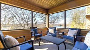 A covered outdoor seating area with wicker furniture and a view of trees and a building in the background. - The Cozy Lake Stay You've been Craving - Fireplace, Comfy Beds & Quiet! (Galena)