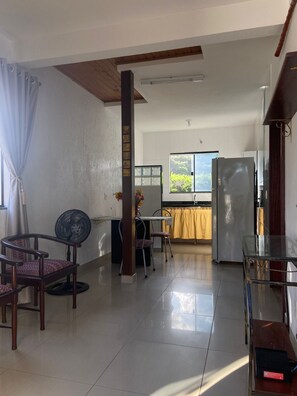 Ampla sala de estar com mesa de jantar, cadeiras, geladeira e ventilador.