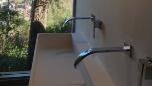 Une salle de bain avec un lavabo blanc, un robinet chromé et une fenêtre donnant sur une forêt.