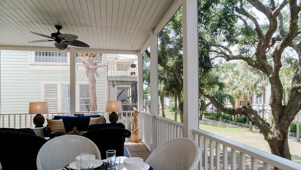 A covered outdoor dining area with a table set for four, a ceiling fan, and a view of a residential neighborhood with trees and houses. - Beautiful Grand Pavilion -  steps to the beach with Grand Pavilion Pool Access (Isle of Palms)