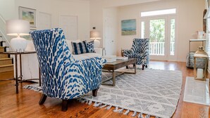 A spacious living room with a large window, a fireplace, and a staircase leading to an upper level. - Beautiful Grand Pavilion -  steps to the beach with Grand Pavilion Pool Access (Isle of Palms)