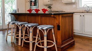 A kitchen with a wooden island, bar stools, a chandelier, and white cabinetry. - Beautiful Grand Pavilion -  steps to the beach with Grand Pavilion Pool Access (Isle of Palms)