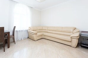 A corner living room with a beige leather sofa, a wooden dining table with chairs, and a radiator.