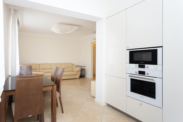 A modern kitchen with white cabinets, a Bosch oven, and a dining area with a wooden table and chairs.