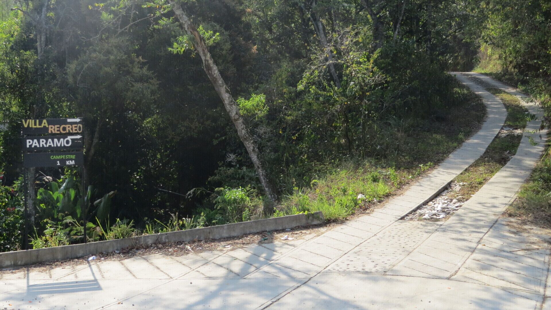 Un chemin pavé traverse une zone boisée et un panneau indique la direction de Villa Recreo et de Paramo, ainsi qu’un indicateur de distance indiquant que le campement de Campestre se trouve à 1 km.