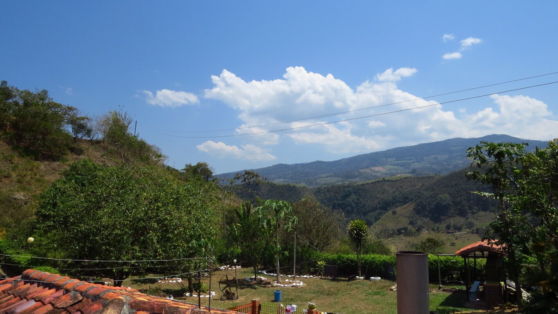 A rural landscape with a view of distant hills, a small building with a red roof, and a clear blue sky.