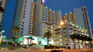 A multi-story hotel with a prominent lit sign, multiple parking structures, and palm trees in the foreground.