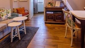 Uma sala de estar aconchegante com piso de madeira, escada branca, mesa de jantar e sofá com almofadas.