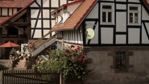 Um edifício tradicional em estilo de enxaimel, com telhado inclinado, chaminé visível e uma pequena janela com um letreiro.