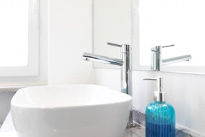 A bathroom with a white sink, chrome faucets, and a blue soap dispenser. - Gasthaus zur Blume (Efringen-Kirchen)