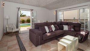 Un salón espacioso con un amplio sofá modular, una mesa de centro y un ventanal de vidrio que da a un patio con piscina.
