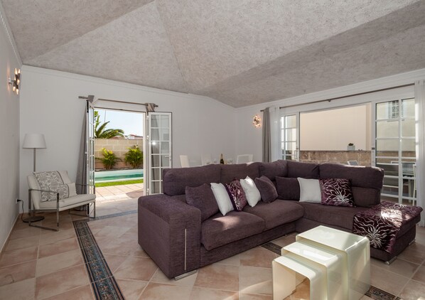 A spacious living room with a large sectional sofa, a coffee table, and a glass door leading to a patio with a pool.