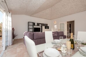 A modern dining area with a white table set for two, a purple sofa, and a bottle of champagne.