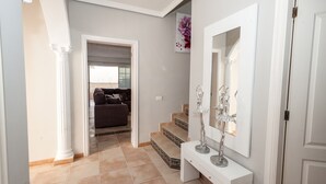 Un pasillo con una escalera que conduce a una sala de estar, una consola blanca con un espejo y una puerta a la derecha.