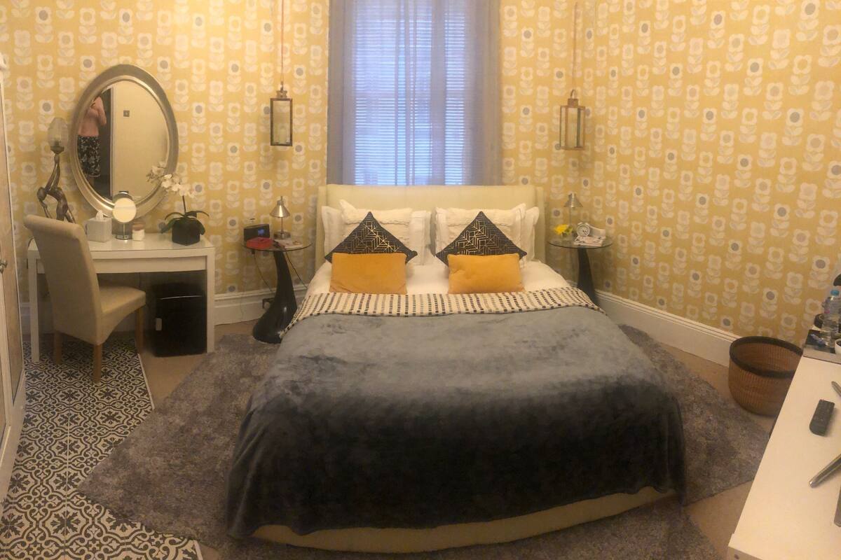 A bedroom with a bed, bedside table, lamp, and a mirror.