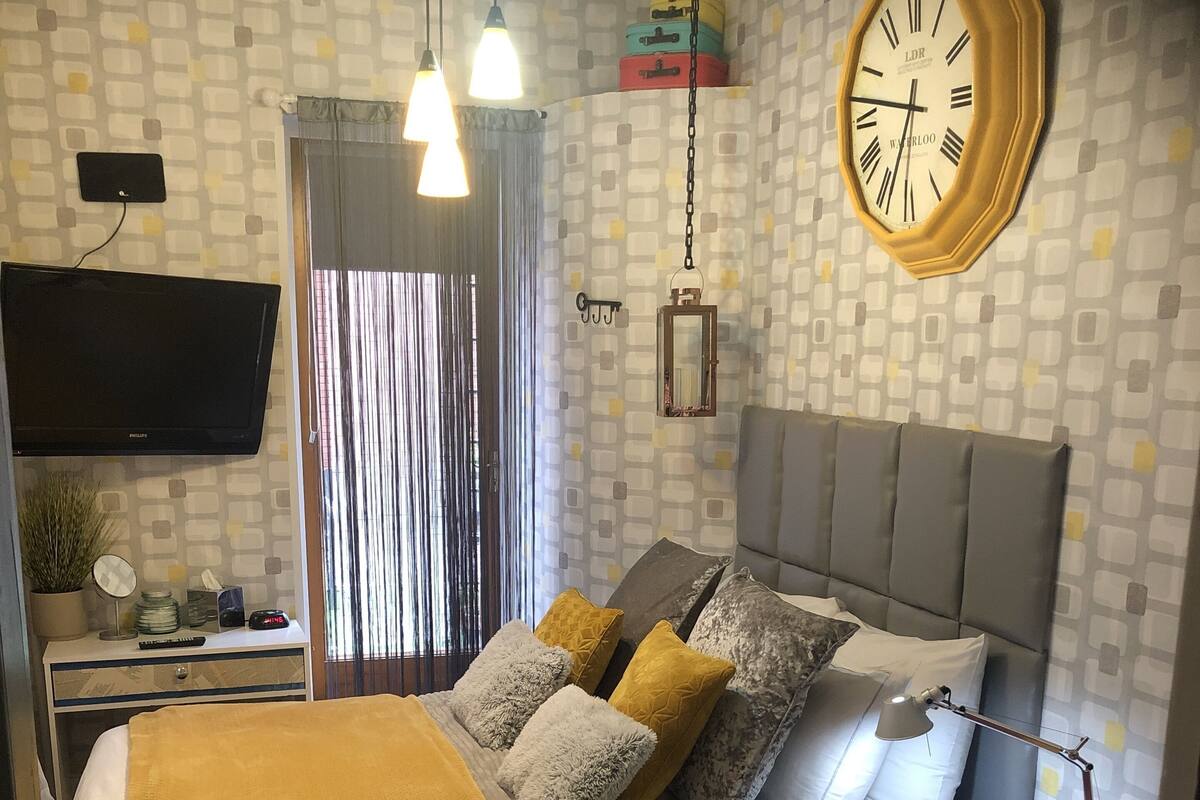 A bedroom with a bed, bedside table, lamp, and a clock on the wall.