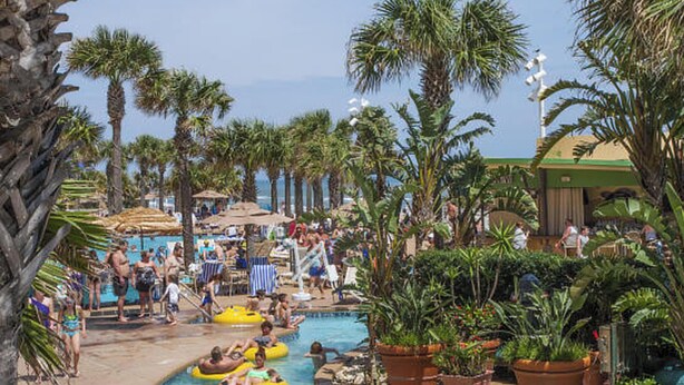 A pool area with multiple lanes for water activities, surrounded by palm trees and shaded by large umbrellas. - Ocean Walk Resort 1709ii Unbelievable Ocean Front Balcony (Daytona Beach)