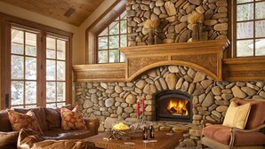 Una chimenea de piedra con fuego, un sofá de cuero y una mesa de centro de madera en una habitación con ventanas amplias.