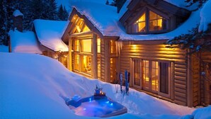 Una cabaña de troncos con jacuzzi y equipo de esquí en la nieve.
