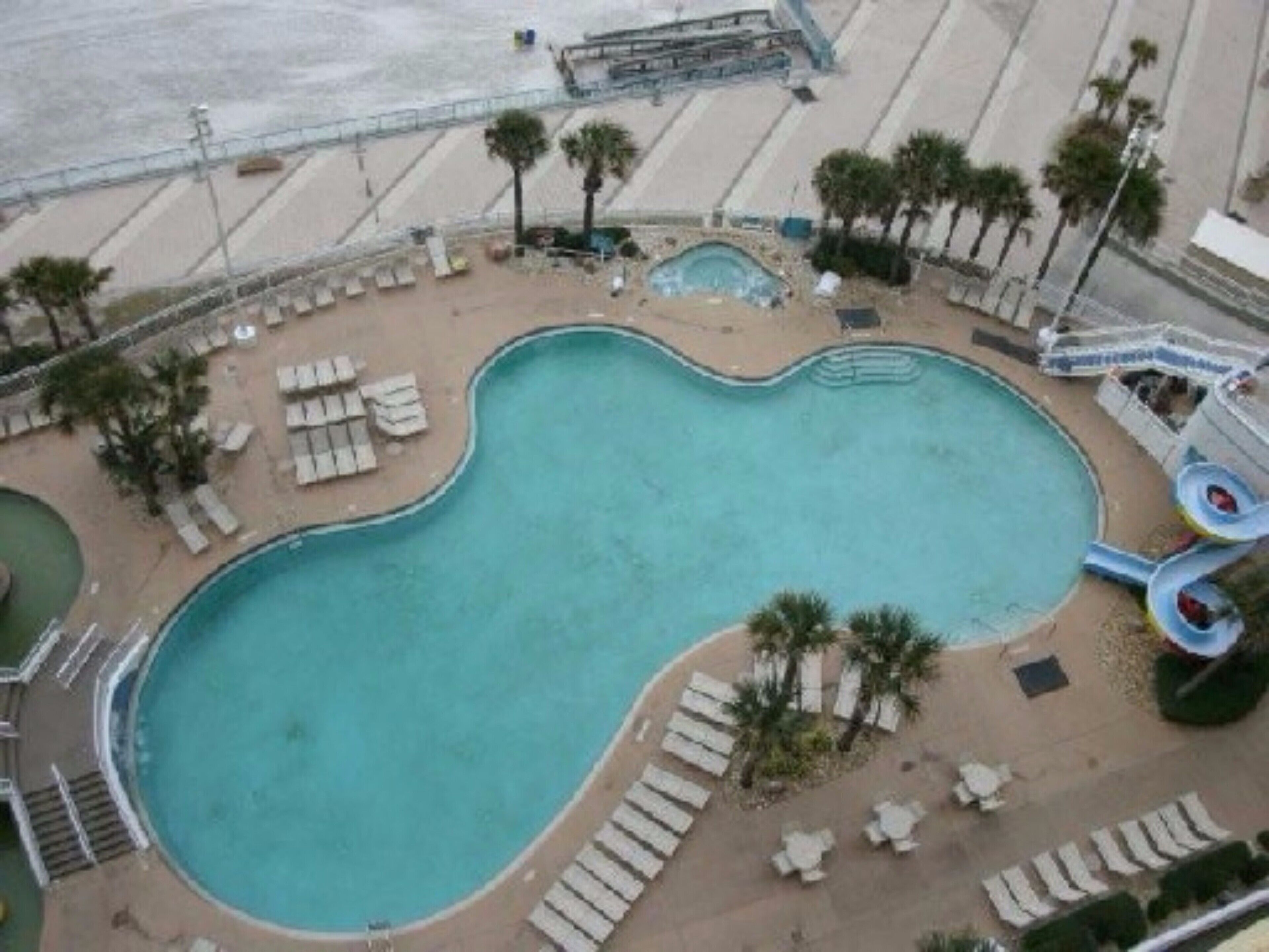 A large, kidney-shaped pool with a small hot tub, surrounded by lounge chairs and palm trees.