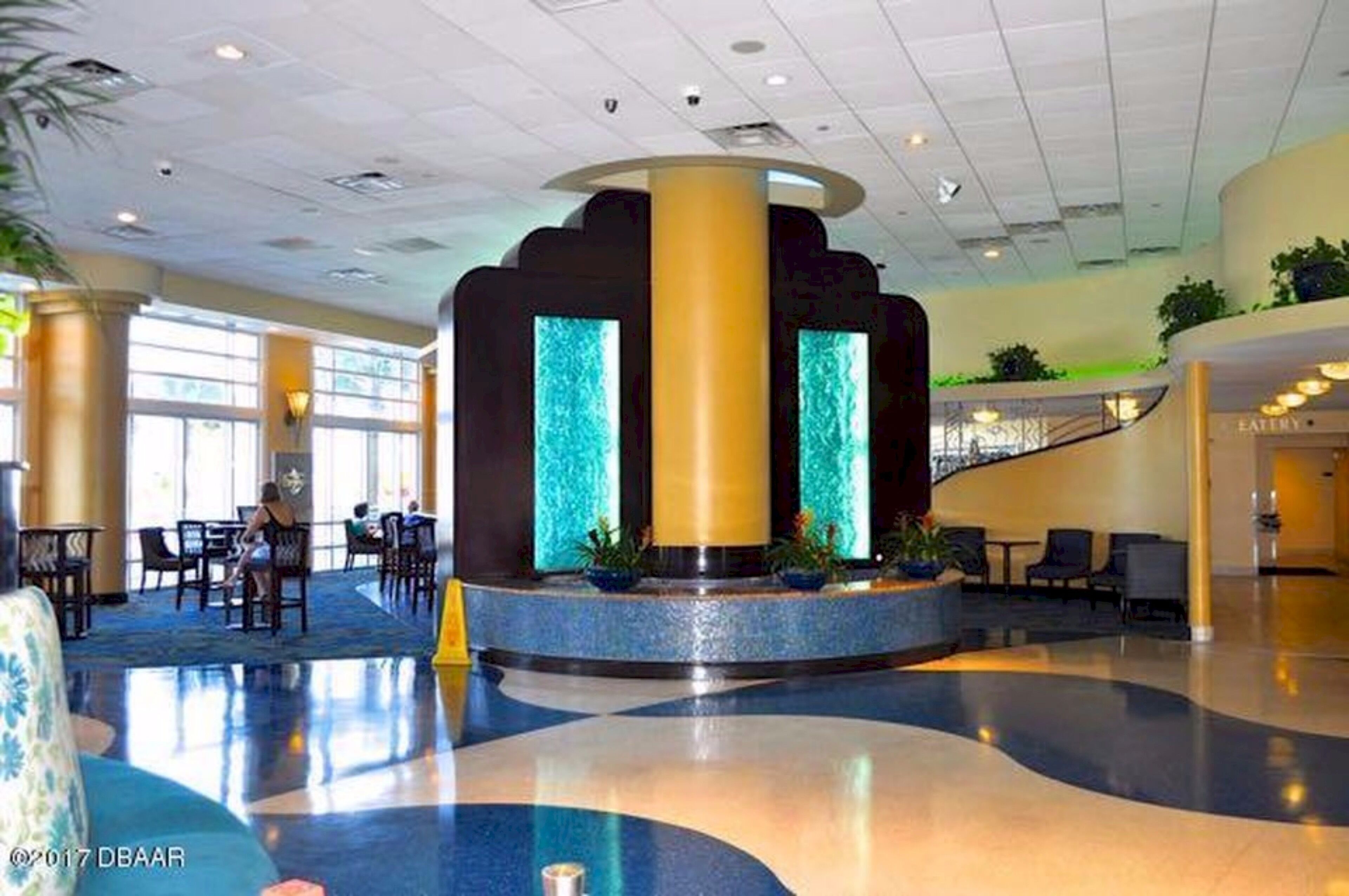 A spacious lobby with a central water feature, seating areas, and a staircase leading to upper levels.