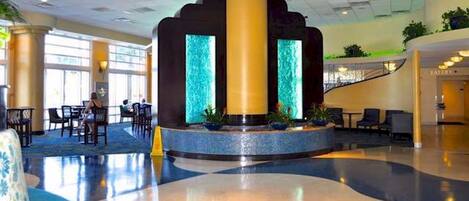 A spacious lobby with a central water feature, seating areas, and a staircase leading to upper levels.