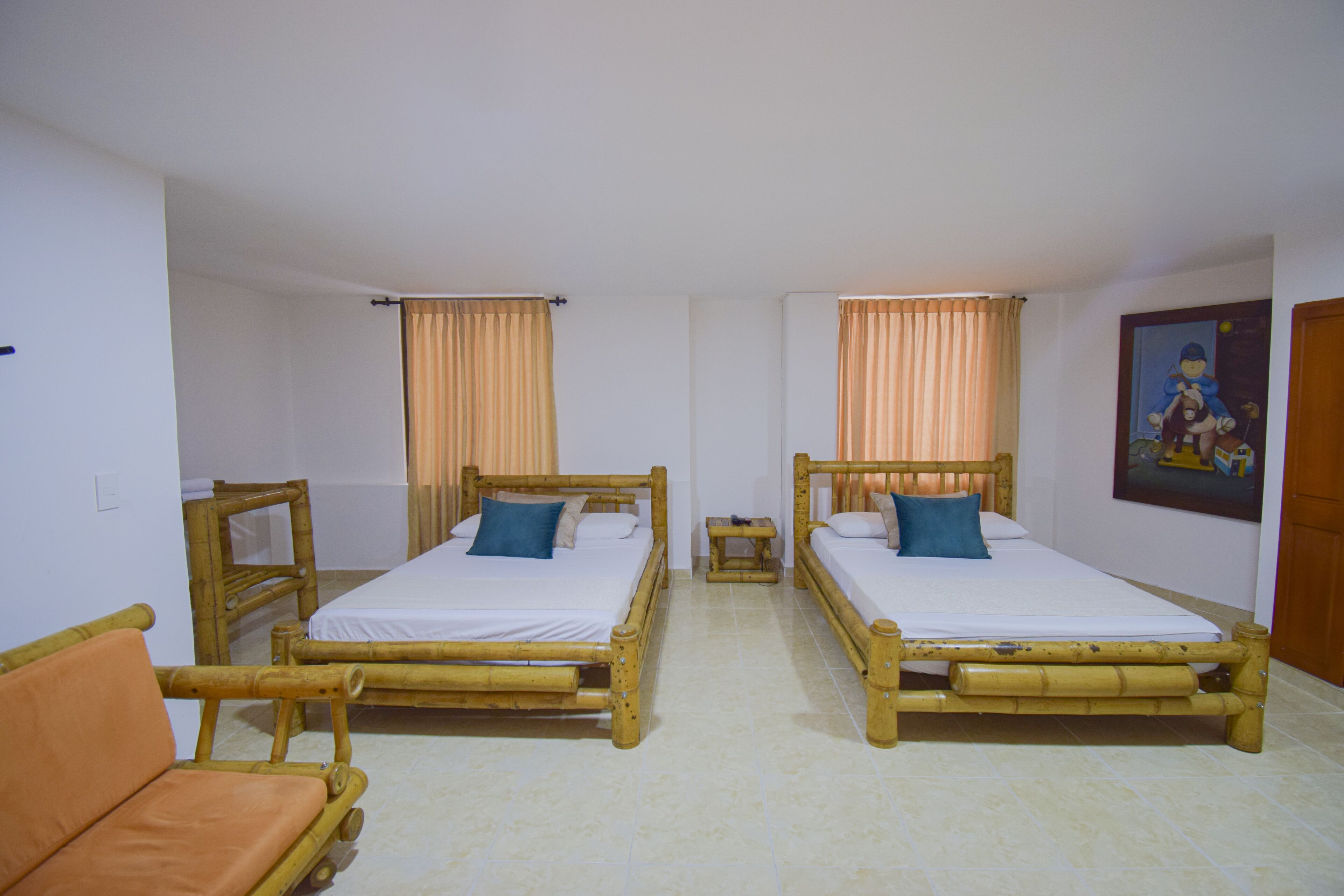 A room with two wooden beds, a small table, a chair, and a painting on the wall.