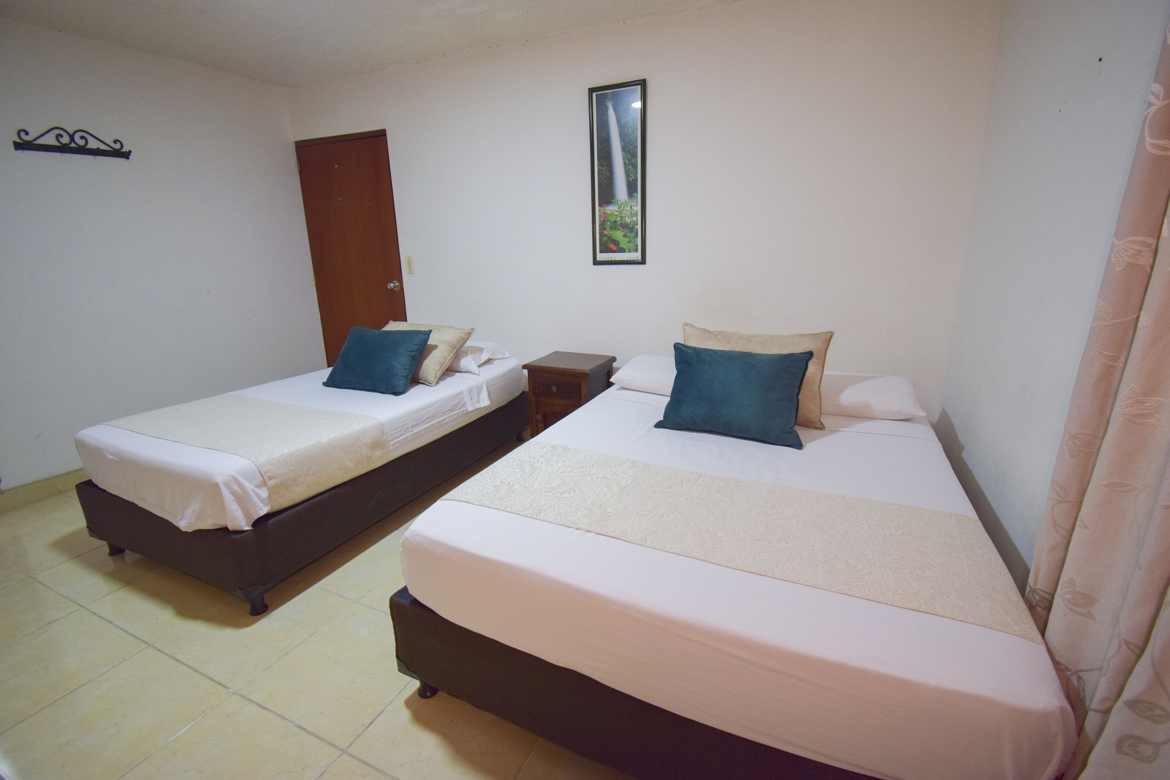 A room with two beds, a wooden door, a framed picture on the wall, and a curtain on the right side.