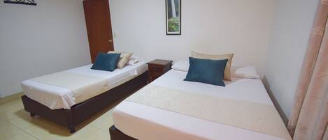 A room with two beds, a wooden door, a framed picture on the wall, and a curtain on the right side.