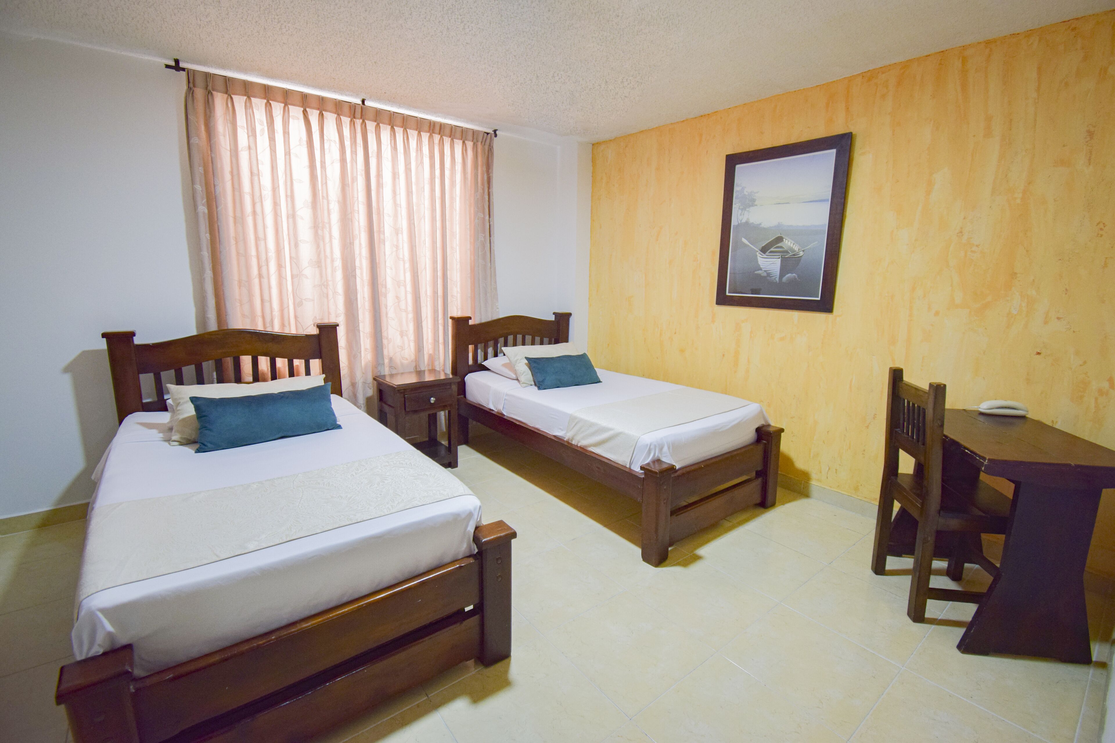 A room with two wooden beds, a small table, and a chair.