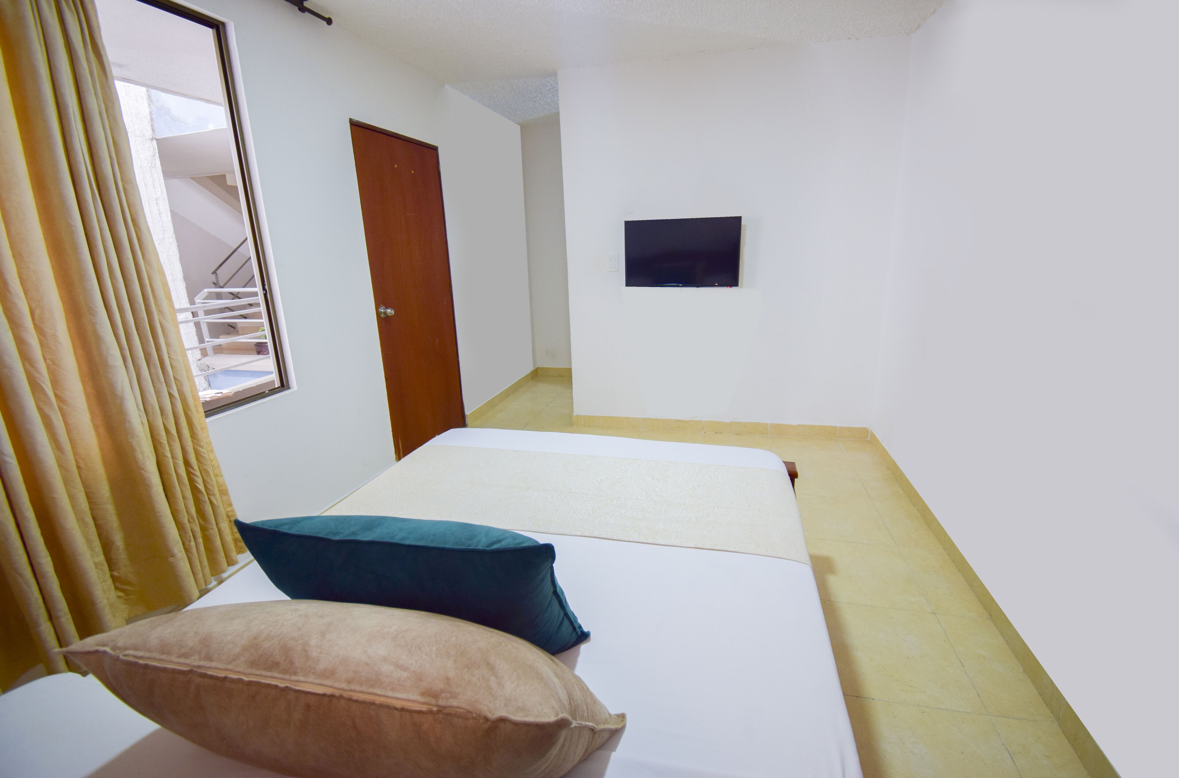Ein Hotelzimmer mit Bett, zwei Kissen, einem Fenster mit Vorhängen, einer Tür und einem kleinen Fernseher an der Wand.