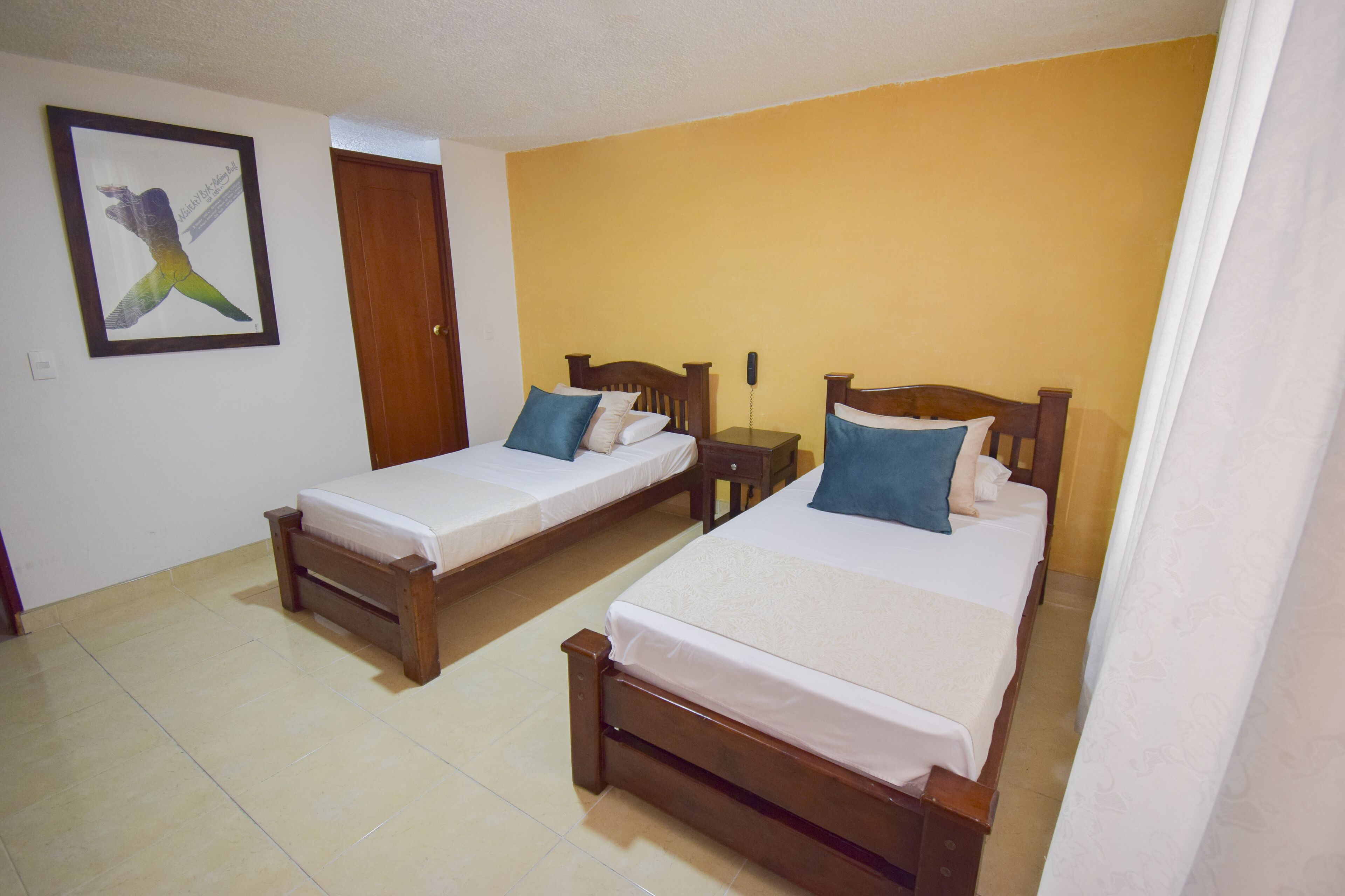 Una habitación con dos camas de madera, una mesita de noche también de madera, un teléfono y un cuadro en la pared.