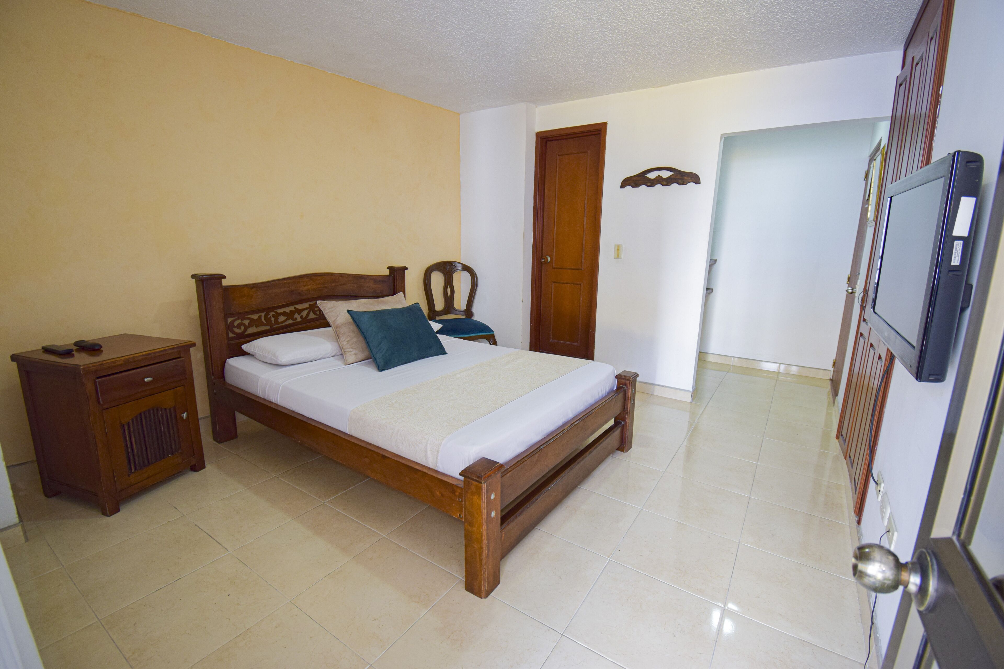 A bedroom with a wooden bed, a nightstand, a chair, a door, and a television.