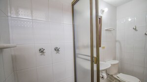 Ein Badezimmer mit weißen Fliesen, einer Toilette, einer Duschkabine und einem Toilettenpapierhalter.