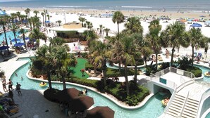 Een resort met een zwembad, palmbomen en uitzicht op het strand.