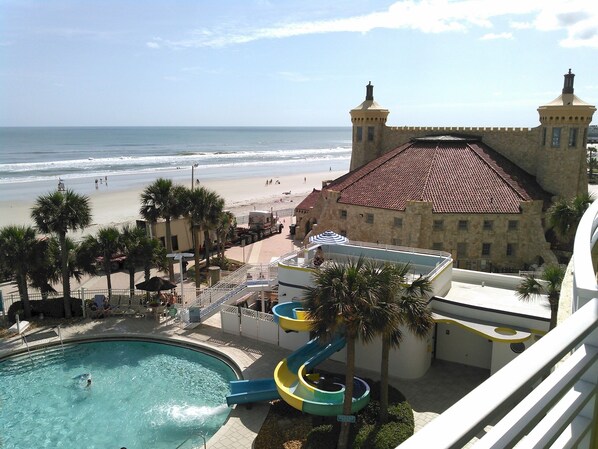 A resort with a swimming pool, water slides, a beach, and a castle-like building.