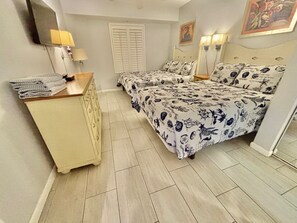 Une chambre avec deux lits, une commode, une lampe et une fenêtre avec des volets.
