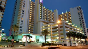 A multi-story hotel with a prominent lit sign, multiple parking structures, and palm trees in the foreground. - Ocean Walk Resort 1305 w/Private Ocean Front Balcony (Daytona Beach)