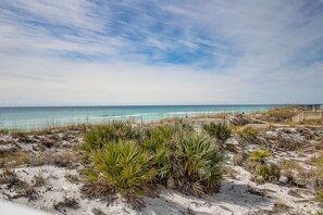 Una playa con dunas de arena, vegetación escasa y un camino de madera que conduce al océano.