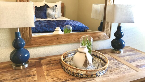 A bedroom with a bed, two lamps, a mirror, and a bedside table with a decorative tray.
